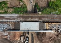 Z perspektywy lotu ptaka pionowy widok na nowo budowany wiadukt kolejowy w Suchedniowie. Widoczne są betonowa konstrukcja obiektu, tory kolejowe przebiegające nad wiaduktem, pale fundamentowe oraz teren przygotowany do dalszych prac budowlanych.