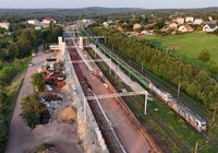 Z perspektywy lotu ptaka widok na modernizowaną stację Łączna. Widoczne są nowe perony, budowana kładka dla pieszych z szybami wind, plac budowy oraz pociąg towarowy na sąsiednim torze.
