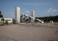 Z perspektywy centralnej widok na budowaną kładkę dla pieszych. Widoczne są dwa żelbetowe szyby wind, konstrukcja schodów oraz teren stacji przygotowany do dalszych prac budowlanych.