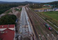 Z perspektywy lotu ptaka widok na modernizowaną stację Zagnańsk. Widoczne są nowe perony, układ torów, pociąg towarowy oraz prowadzone prace budowlane w otoczeniu stacji.