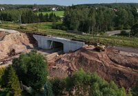Z perspektywy lotu ptaka widok na nowy wiadukt drogowy pod linią kolejową w Łącznej. Widoczne są tory kolejowe, betonowa konstrukcja obiektu, koparka, wykopy oraz teren prowadzonych robót ziemnych.