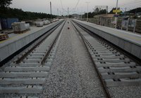 Z perspektywy centralnej widok wzdłuż nowo budowanych torów pomiędzy peronami stacji Zagnańsk. Widoczne są nowe nawierzchnie peronów, oznakowanie, elementy infrastruktury oraz przygotowane materiały budowlane.